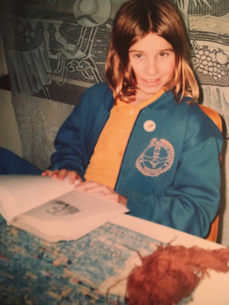 Photograph of child in school uniform reading a book on a kitchen table
